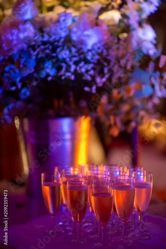 Sparkling wine glasses on wedding reception table with floral decoration and colorful bokeh lights