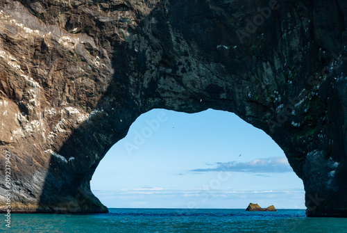 Dyrhólaey sea arch in South Iceland with dramatic basalt cliffs rugged Atlantic coastline and spectacular volcanic rock formations beneath a clear blue sky