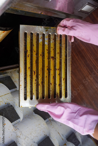Housekeeping hands trying to removing a filters from cooker hood or chimney for cleaning. Replacing filter in modern kitchen hood or kitchen chimney maintenance for kitchen appliance.