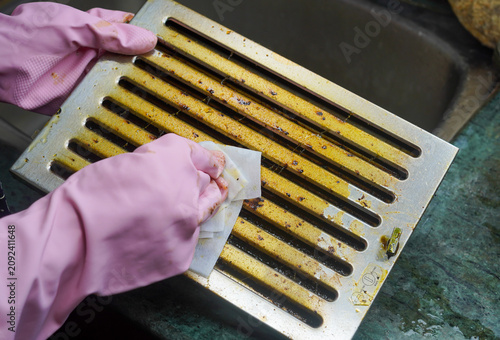 Woman pink gloves hands put stained oily dirty filters of cooker hood or kitchen chimney in sink before cleaning by sponge. Hygiene maintenance concept.