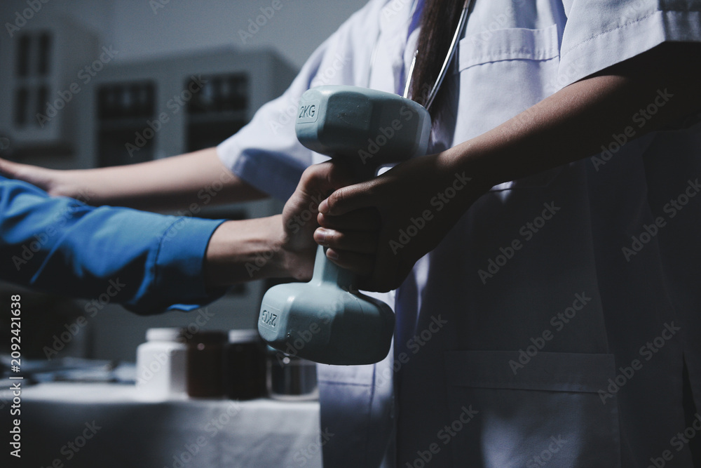 Naklejka premium A healthcare professional (physiotherapist) assists a patient with arm rehabilitation exercise using a dumbbell. Focus on recovery and physical therapy