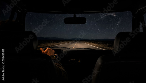 A male driver holds the steering wheel while driving along an empty highway under a starry night sky.