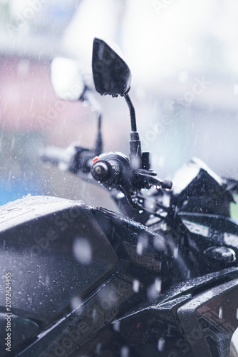 Closeup of a motorcycle handlebar and fuel tank during a heavy rainstorm, capturing the texture of raindrops on the dark metallic surface