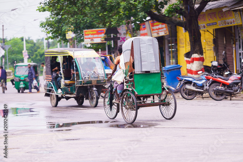 Fotografía A rickshaw puller driving a cycle rickshaw on a busy street in india with auto r