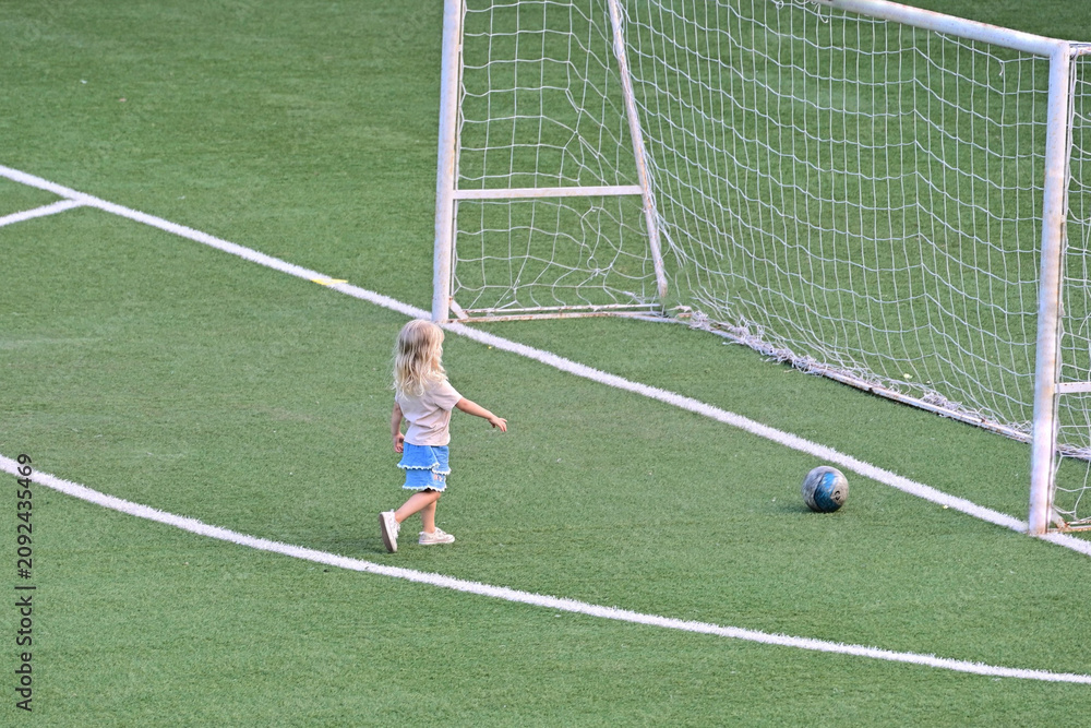 Fototapeta premium unrecognizable blonde female child playing alone on soccer football pitch