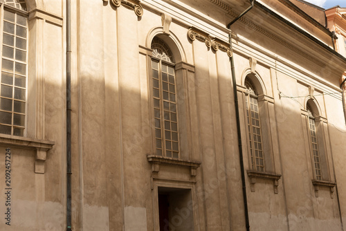Foto Exterior view of a historic stone building facade featuring tall arched windows with muntins, decorative cornices, pilasters, and a recessed doorway