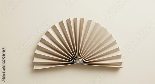 A semi-circular folded paper fan with accordion pleats on a solid light beige background