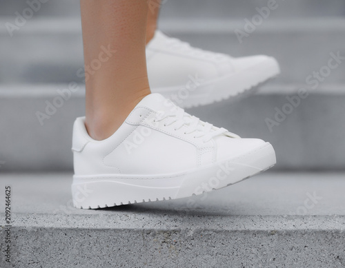 Climbing stairs outdoors in white sneakers with elegant laces, low heel, and textured sole, showcasing casual footwear in a concrete environment from a lower viewpoint