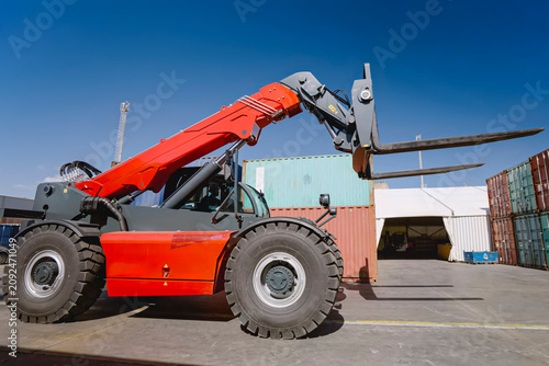 Orange Telehandler Lifts Its Forks Beside Stacked Shipping Containers at a Port Yard
