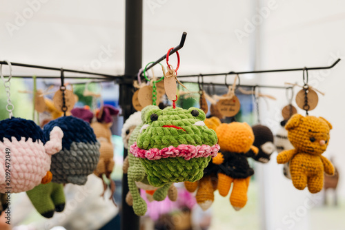 Cute handmade crochet frog keychain hanging on display at an artisan market.