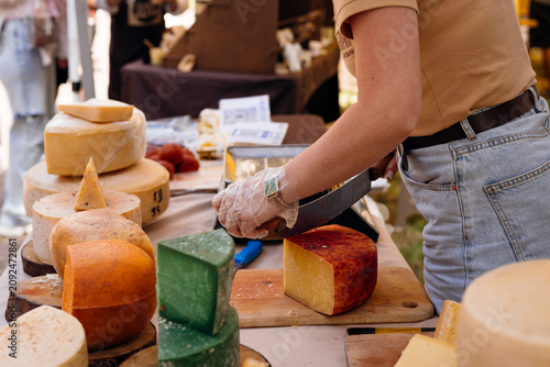 Vendor slicing a wheel of artisan cheese at a local farmers market.