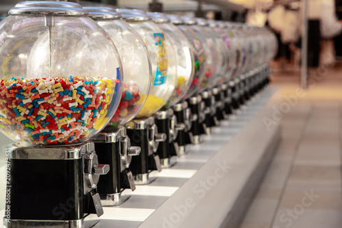Retro mechanical candy and gumball vending machines lined up on an urban sidewalk, offering treats to pedestrians in a public commercial district.
