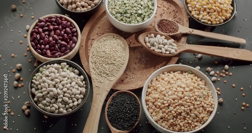Colorful selection of raw uncooked legumes and grains displayed in bowls and spoons on a dark surface, highlighting various types of healthy plant-based protein sources for a balanced diet.