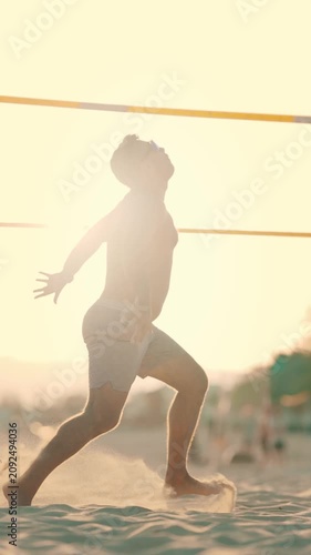 Man plays beach volleyball at sunset on sandy beach, engaging in fun activity with friends