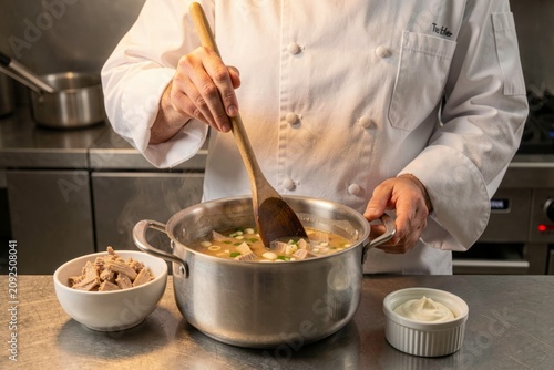 Ciorba de Burta being prepared in modern kitchen by chef stirring pot with wooden spoon. Concept of culinary art, showcasing tripe soup with garlic vinegar cream preparation.