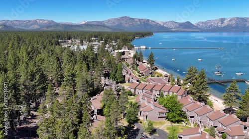 Aerial drone tracking shot flying forward over a Lake Tahoe beachside community with vacation properties, houses, and boats moored in the marina