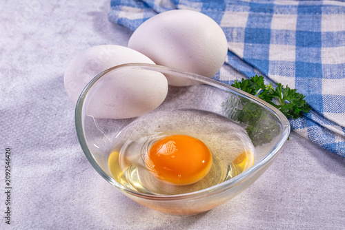 Raw egg in glass bowl with whole eggs and parsley on checkered cloth