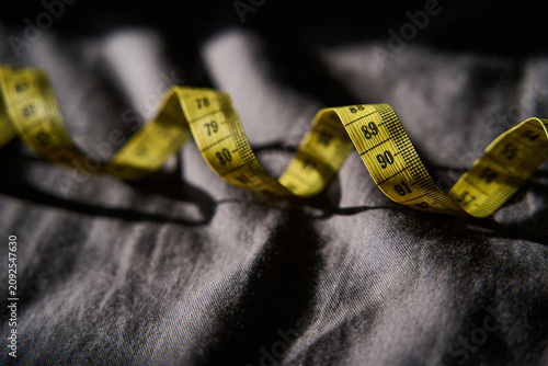 Foto Measuring Tape Coiled Resting On Wrinkled Dark Fabric Surface With Strong Directional Low Light And Shallow Depth Of Field For Closeup Detail