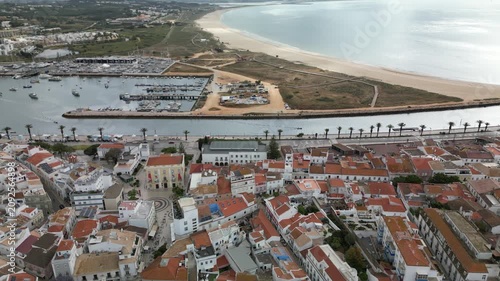 High-altitude drone footage of Lagos, Portugal, with city, sea, marina, sandy beach, rooftops and cloudy coastal atmosphere, perfect for destination marketing.