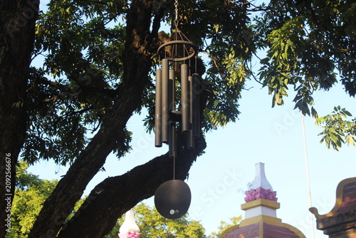 Bild auf Leinwand Large dark wind chimes hanging from tree branch near temple roof in sunny garden