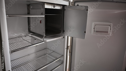 Картината върху платно Interior of an empty vintage 1940s or 1950s white refrigerator with wire shelves and open freezer compartment