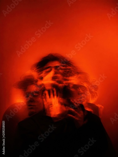 Ethereal triple exposure portrait of an anxious anonymous man with distorted features and motion blur, intense saturated crimson neon lighting for psychological editorial storytelling