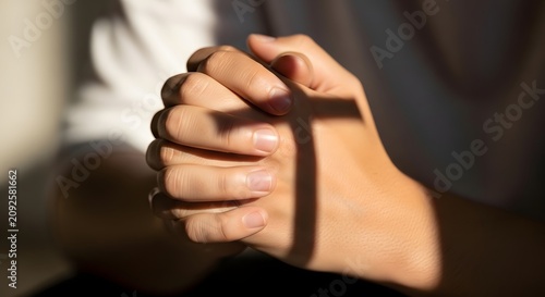 Close-up of human hands folded in prayer with a shadow of a christian cross cast over them as a symbol of faith and hope, religion