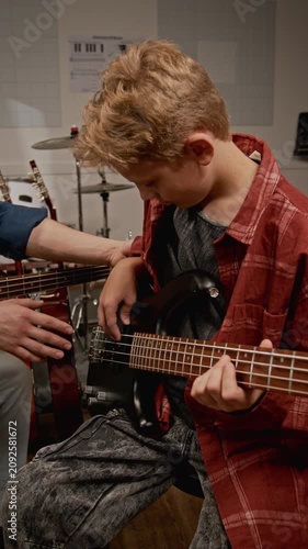 Vertical video of Caucasian young male music teacher instructing Caucasian teenage boy on playing bass guitar in studio. Clip for music school ads
