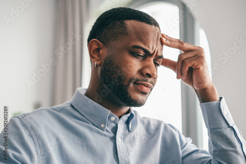 Cuadro en lienzo Young adult man gripping his forehead tightly, expressing intense pain and frust