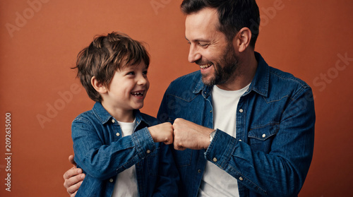 A cheerful father and young son share a playful fist bump in a studio setting, symbolizing teamwork, trust, friendship, and positive family connection.