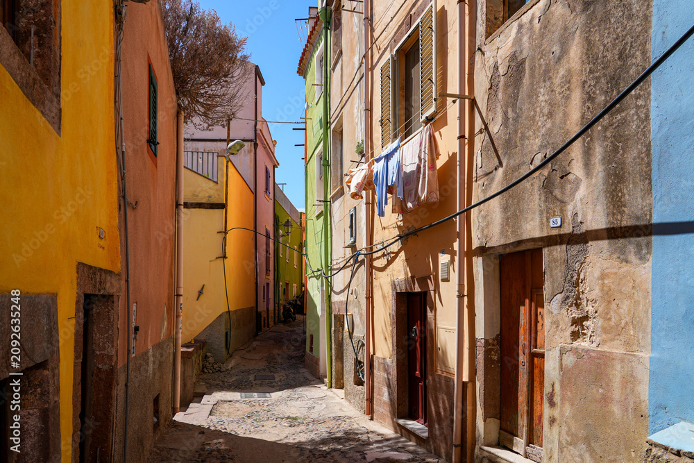 Fototapeta premium Narrow cobblestone street lined with colorful houses in the historic town of Bosa, Sardinia, Italy