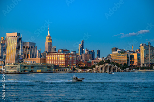 Midtown Manhattan skyline and Little Island park at twilight. Security boat cruising on the Hudson River past illuminated New York skyscrapers and landmarks.