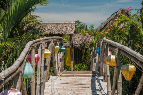 Traditional bamboo footbridge decorated with colorful lanterns in a tropical eco village