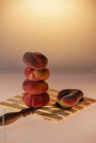 Flat peaches stacked in a tower resting on wooden spoons on a warm amber background. Creative still life with fruit and kitchen utensils, copy space.