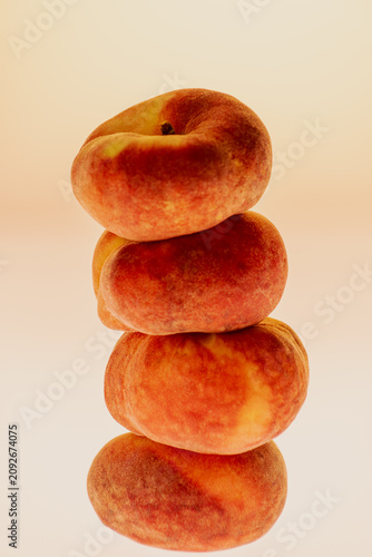 Three flat peaches stacked vertically in a tower on a warm gradient background. Clean studio still life with copy space, vertical composition.