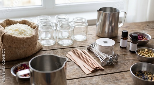 Candle making supplies including wax flakes melting pitchers wicks and essential oils on table