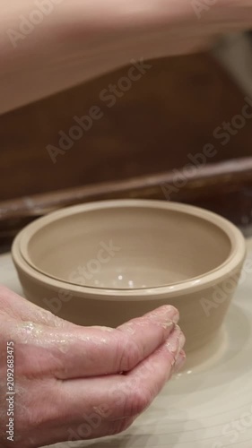 Close-up of muddy hands shaping a wet beige clay bowl on a spinning pottery wheel in an artisan workshop, representing creative ceramic art craft and handmade hobby.
