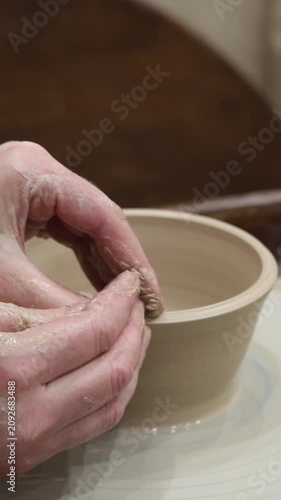 Closeup skilled muddy hands shaping wet beige clay pot on spinning pottery wheel, artisan molding ceramic cup with dirty fingers in craft workshop studio, creative art therapy relaxation process hobby