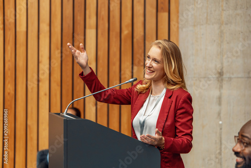 Woman business speaker giving confident conference presentation at podium with microphone