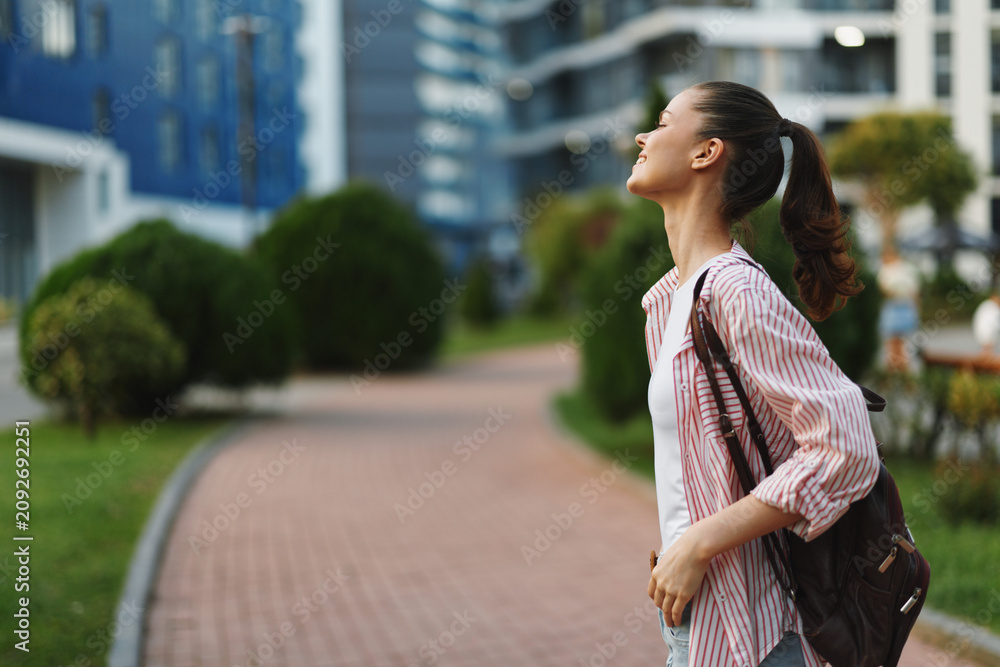 Naklejka premium Young student woman with backpack standing outdoors in an urban campus setting, looking up with curiosity, capturing lifestyle, study focus and confidence.