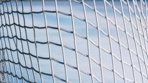 Close-up shot of white braided nylon hockey goal net hanging against blurry blue ice surface background