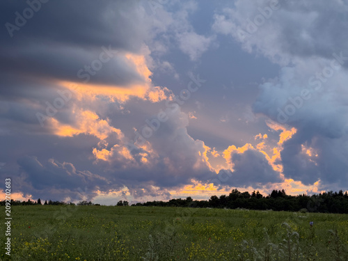 Bright clouds and sunset over a grassy field in a rural area during the evening sky
