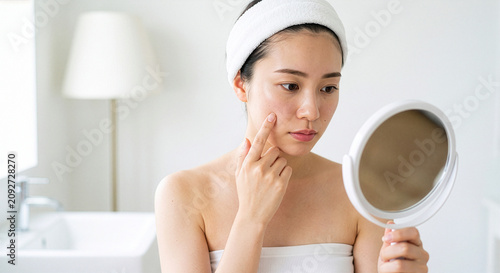 鏡を見ながら肌の調子やニキビを気にする若い日本人女性（スキンケア・肌荒れ）