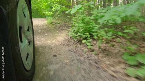 Rural countryside road in the woods drive on the gravel. Cinematic POV of front right car wheel driving plate. Gentle turns on dirt road in the crown land from behind right wheel exterior view.