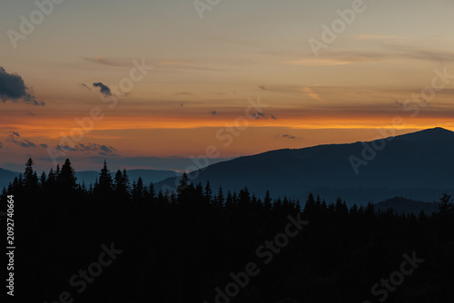 Beautiful evening twilight with bright orange sky above dark mountain ridges.