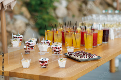 Catering buffet table with sweet mini desserts in cups and refreshing cocktails.