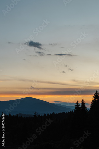 Beautiful evening twilight with bright orange sky above dark mountain ridges.