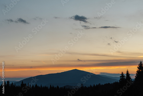 Beautiful evening twilight with bright orange sky above dark mountain ridges.