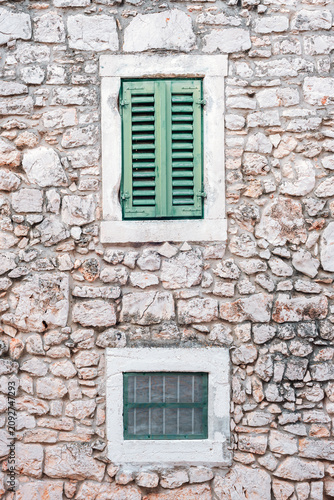 Stone wall with green wooden shutters on an old rustic building facade