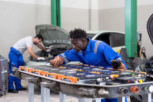 Auto technicians service an electric vehicle battery pack in a garage workshop, performing diagnostics and repairs on lithium power modules at a workbench.